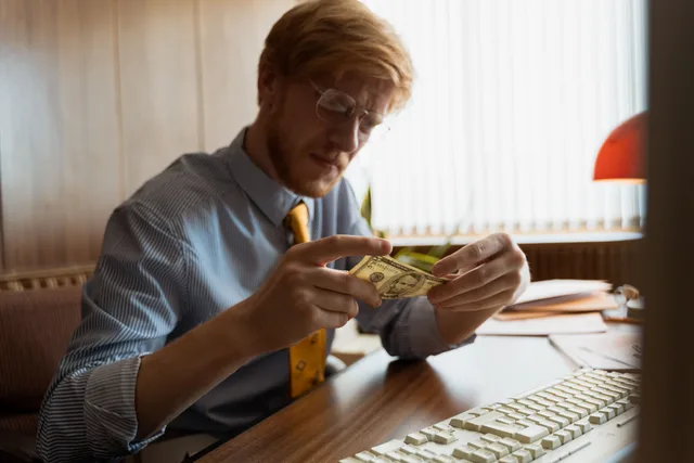 Male entrepreneur intensely examines money at his office desk, representing finance. Celebrity Endorsement Income: Payment Flow Basics
